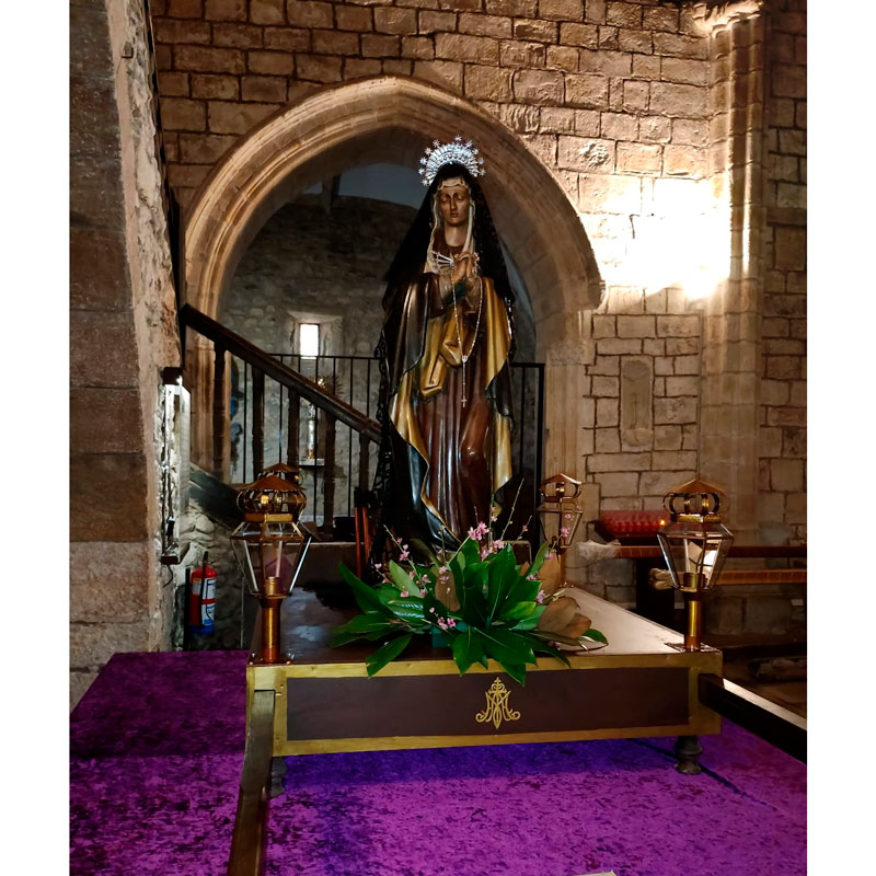 Imagen de la Virgen Dolorosa acompañada por faroles de procesión artesanales en el interior de una iglesia durante la Semana Santa.